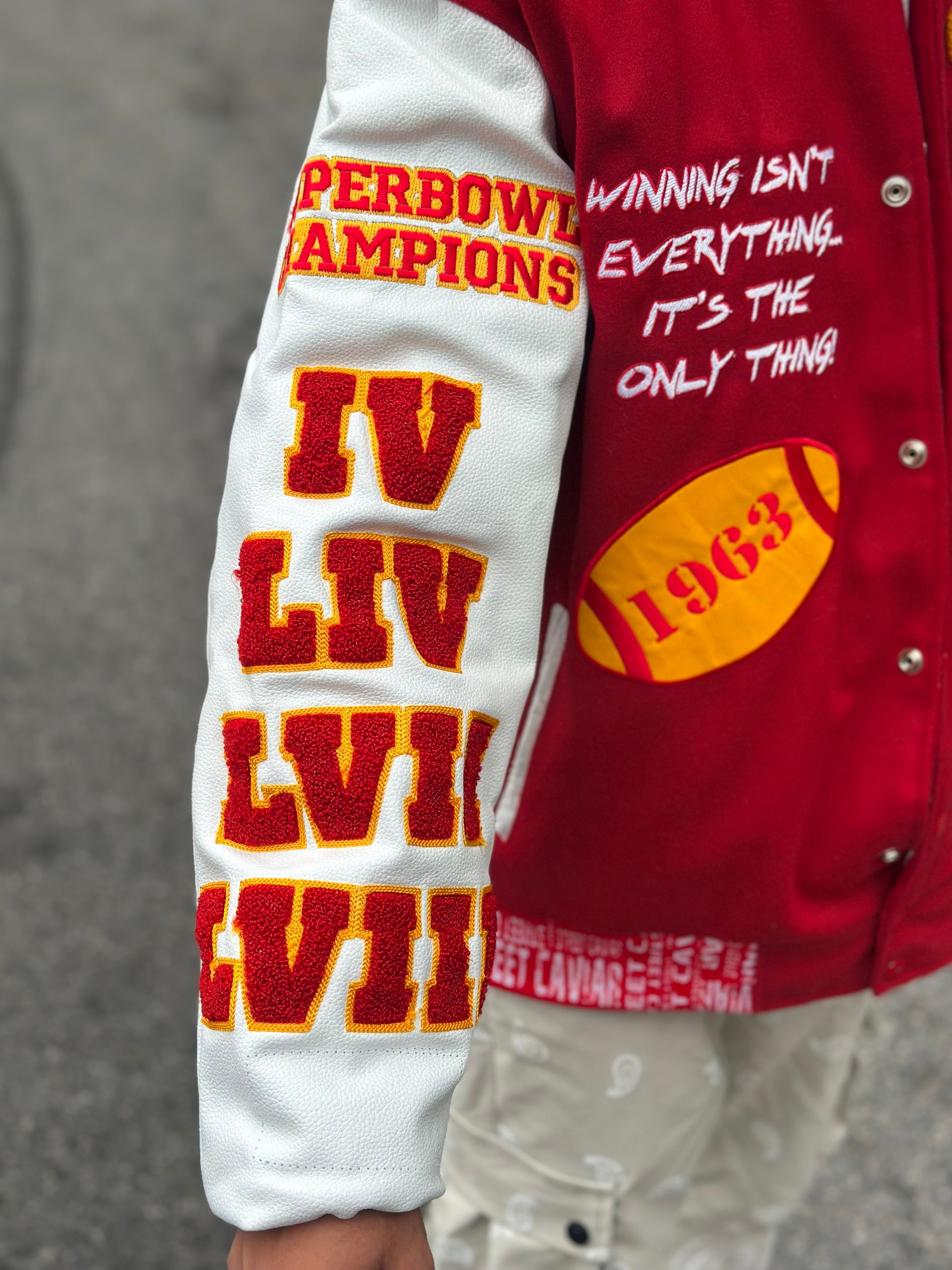 Close-up of Street Caviar KC Chiefs varsity jacket sleeve featuring embroidered “Super Bowl Champions” patch, Roman numerals IV, LIV, LVII, and front chest text reading “Winning isn’t everything… it’s the only thing!” with 1963 football patch.